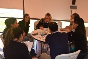 Siete pesonas trabajando en grupo, sentados en una mesa redonda, mientras participan en la Escuela de Evaluación. 