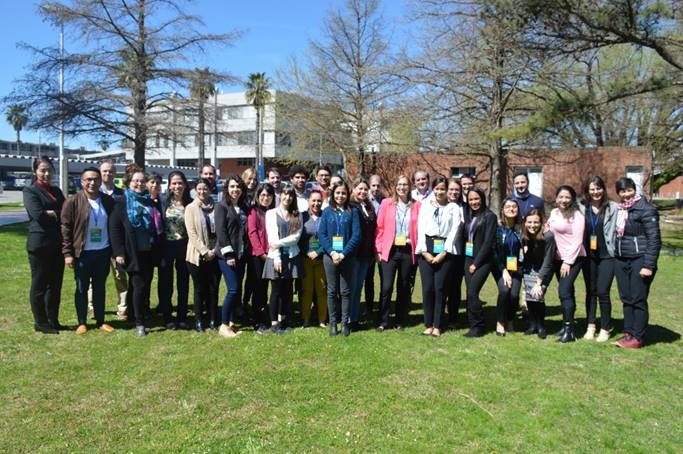 Foto de 32 participantes de la Escuela de Evaluación, posan de pie en un área verde, todos sonríen