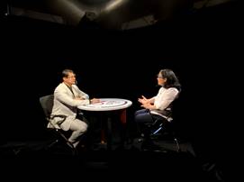 Foto de la Dra. Rosaura Romero en la entrevista con el Dr. Marlon Mora, en un fondo negro una mesa redonda y ellos sentados uno frente al otro, traen mascarillas protectoras conta COVID-19.