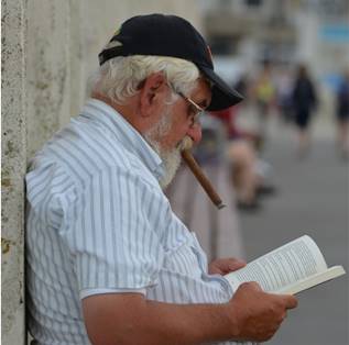 Señor recostardo a la pared fumando un habano, leyendo un libro