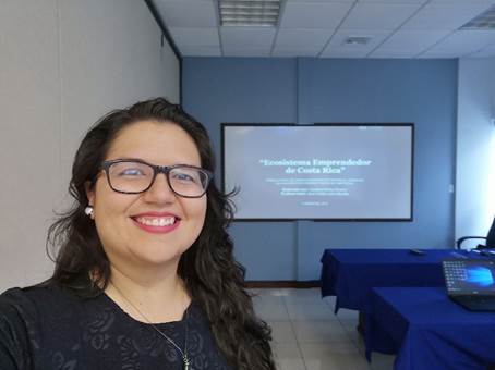 Foto de Catalina Núñez, posando de fondo en una pantalla se proyecta el trabajo de tesis.