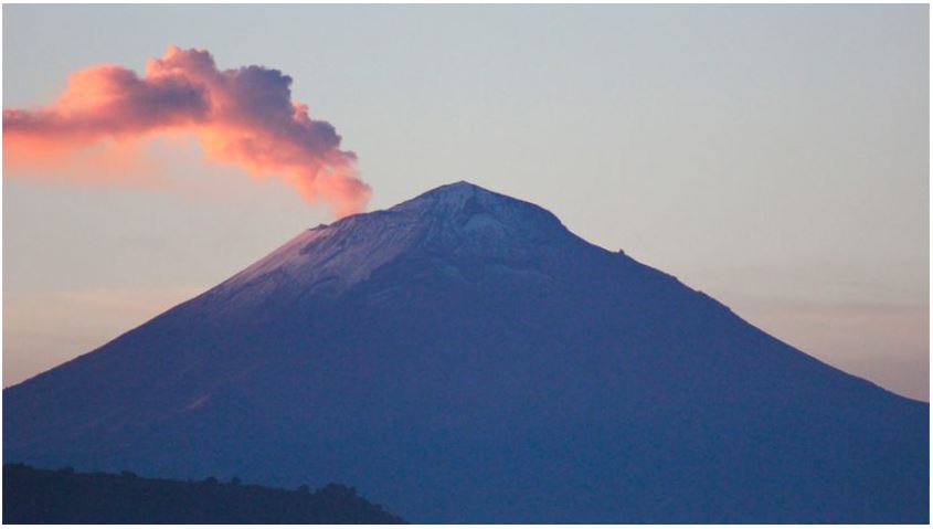 Foto de un volcán mientras emite humo de color rojo.
