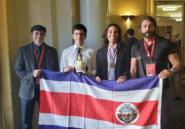 La delegación de Costa Rica posa de pie sosteniendo el Pabellón Nacional, sonríen.