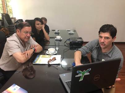 El Máster Max Cerdas y la Ing. Irene Armas del CONICIT conversan con el Dr. Branko Hilje; todos sentados en una mesa y el Dr. Hilje les muestra el proyecto en su computadora.