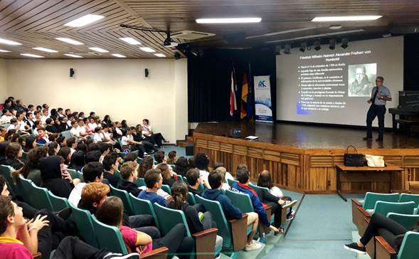 Foto de auditorio donde se impartió la charla, Dr. Alvarado de pie frente al público mientras dictaba su charla.