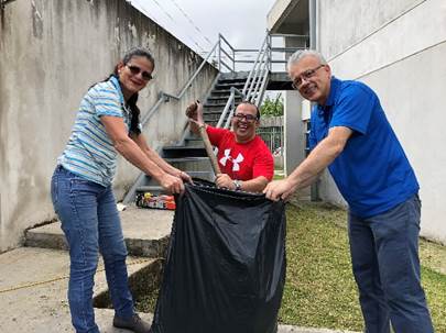 Foto donde Pablo recoge residuos de la limpieza del jardín con una pala, mientras Rocío Vargas y Arturo Vicente sostienen una bolsa de jardín.