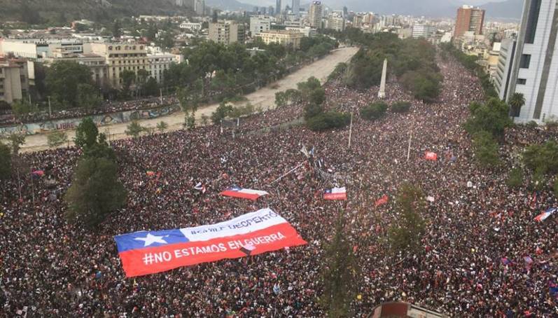Foto aérea de la manifestación pacífica, se logra ver una manta gigante de la bandera de Chile con un el rótulo "#no estamos en guerra".