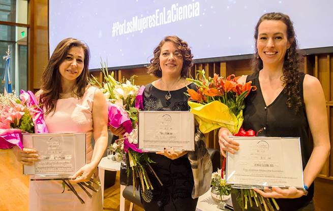 Vanesa Gottifredi (centro), María Fernanda Ledda (izq.) y Marina A. González Besteiro, todas posan con su galardón y un ramo de flores, sonríen. Créditos: CONICET Fotografía.