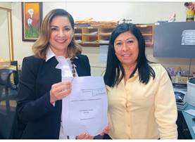 La Diputada Silvia Hernández, posa junto a una representante de la Asamblea Legislativa mostrando el proyecto de ley, ambas sonríen.