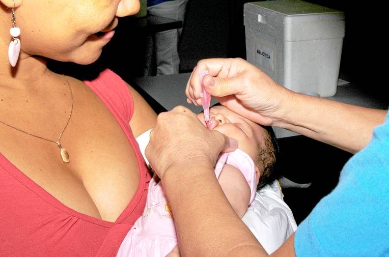 Foto ilustrativa, muestra a una bebé  alzada mientras le dan una vacuna vía oral.