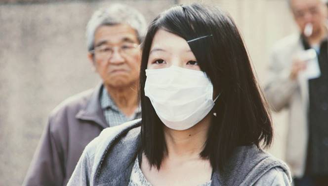 Foto ilustrativa, una chica china en un exterior camina con una mascarilla cubrebocas.