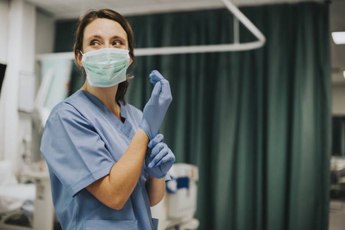 Foto ilustrativa, una enfermera se con una mascarilla cubrebocas, mientra se pone unos guantes de latex.