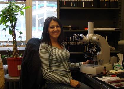 Foto de la Dra. Pamela Murillo, posa sentada en su laboratorio frente a un microscopio