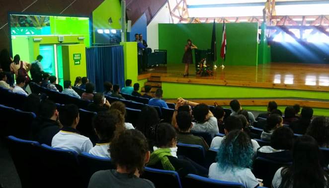 La Dra. María Laura Arias de pie en el podio del auditorio con el microfono brinda la charla y los asistentes sentados.
