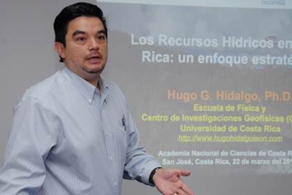 Foto del Dr. Hugo Hidalgo León, cuando impartía charla sobre Recursos Hídricos; de pie frenta a una pantalla que proyecta la charla.