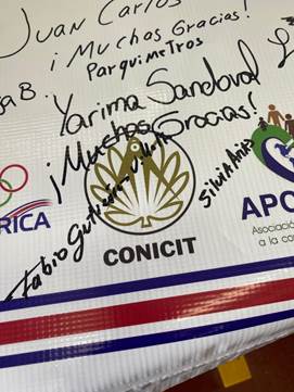 Manta firmada por los representantes de las instituciones asistentes al agradecimiento; en la foto se muestra la sección de la manta donde está el logo del CONICIT y la firma de los representantes del CONICIT asistentes.
