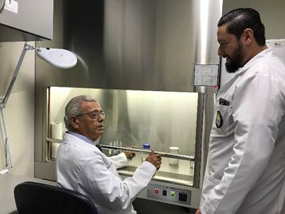 El Dr. Chinchilla sentado en su laboratorio junto a un estudiante de la UCIMED que se encuentra de pie conversando.