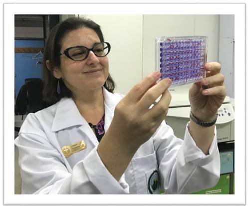 Foto de la Dra. Corrales sentada con gavacha blanca mientras trabaja en el laboratorio, tiene en las manos un serie de muestras.